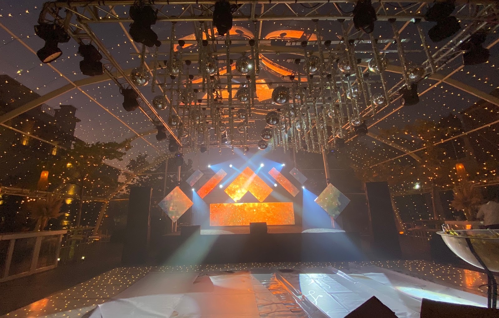 Escenario DJ con frente LED naranja bajo truss con esferas espejadas