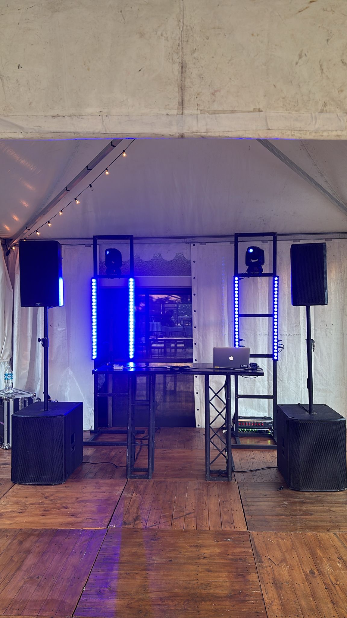 Mesa DJ montada en carpa con parlantes, barras LED y laptop