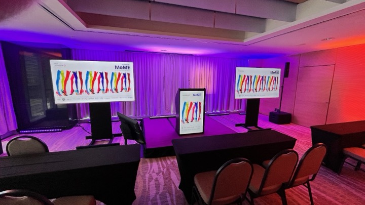 Podio digital con branding del evento flanqueado por pantallas en sala de hotel