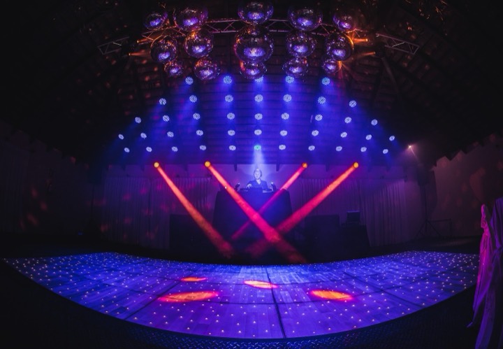 Mesa DJ centro de pista, haces naranjas, esferas espejadas, piso LED