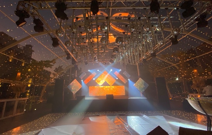 Escenario DJ con frente LED naranja bajo truss con esferas espejadas